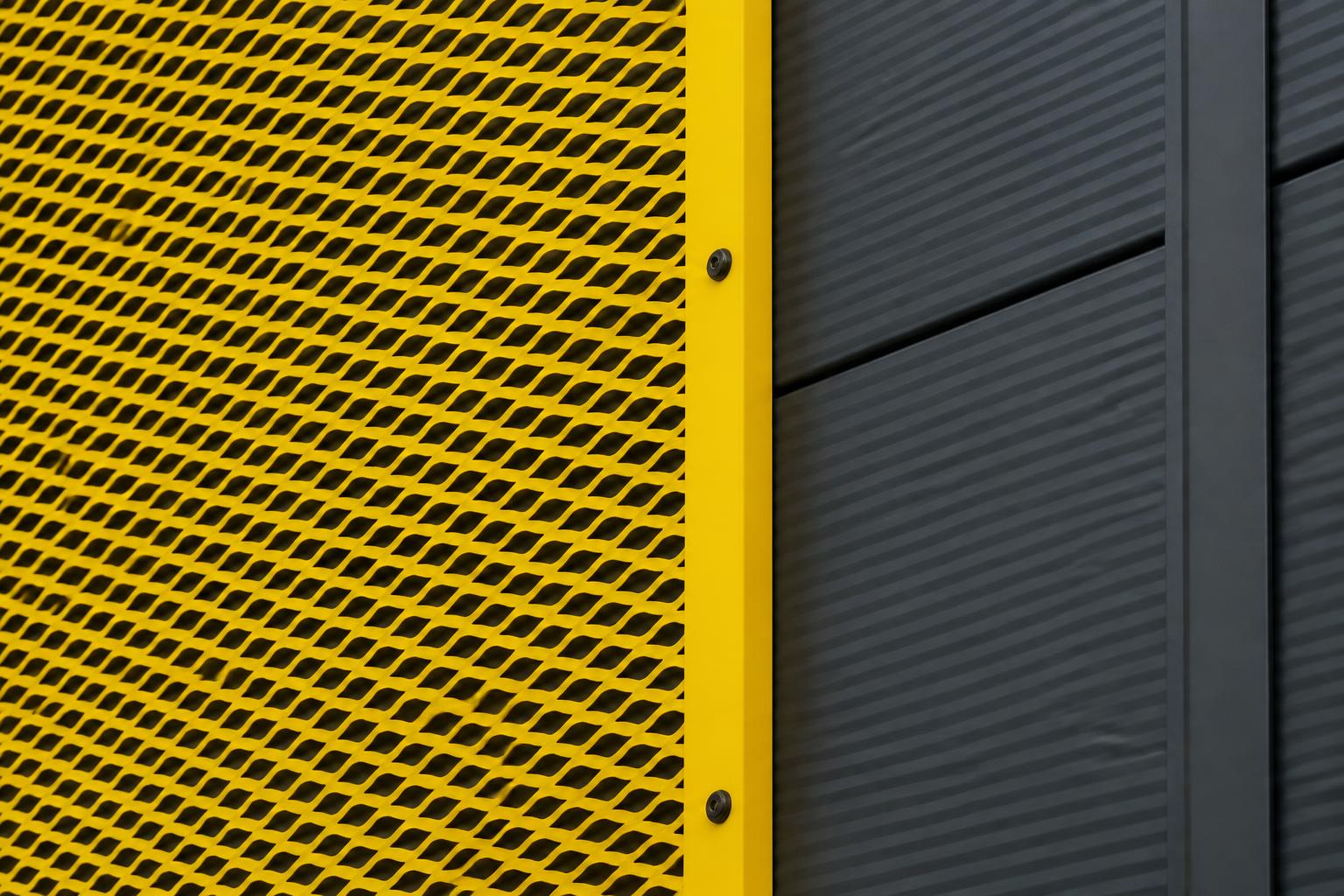 Materiaaldetail van geel strekmetaal tegen antracietgrijze gevelpanelen